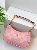 Pink handbag with gold chain strap on a white surface with a plant in the background